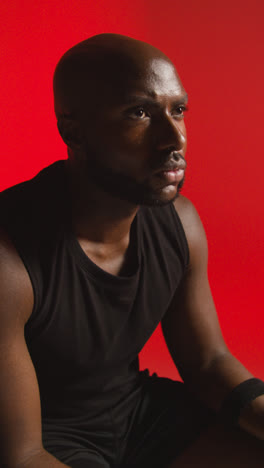 Vertical-Video-Close-Up-Studio-Shot-Of-Seated-Male-Basketball-Player-With-Hands-Holding-Ball-Against-Red-Background-1